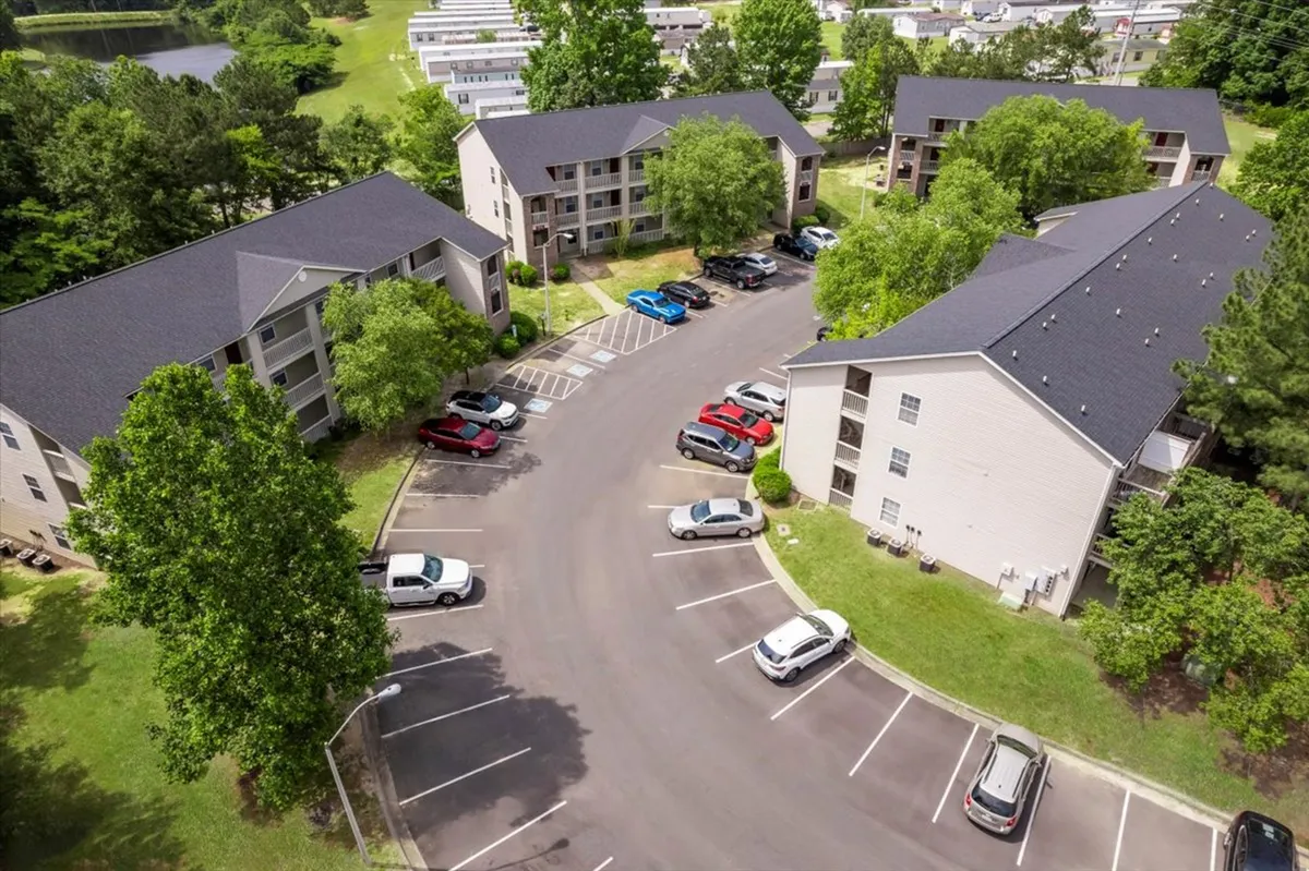 This exterior image displays the apartment buildings nestled among mature trees, with a well-kept parking lot and communal outdoor spaces visible. The setting encourages outdoor activity and interaction among residents, hinting at the inviting green surroundings that blend seamlessly with the local parks and trails described in the section.