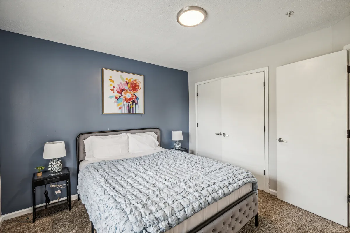 A serene bedroom featuring a plush, inviting bed adorned with soft linens, tasteful wall art, and a cozy nightstand—bathed in calming natural light that creates a peaceful atmosphere.