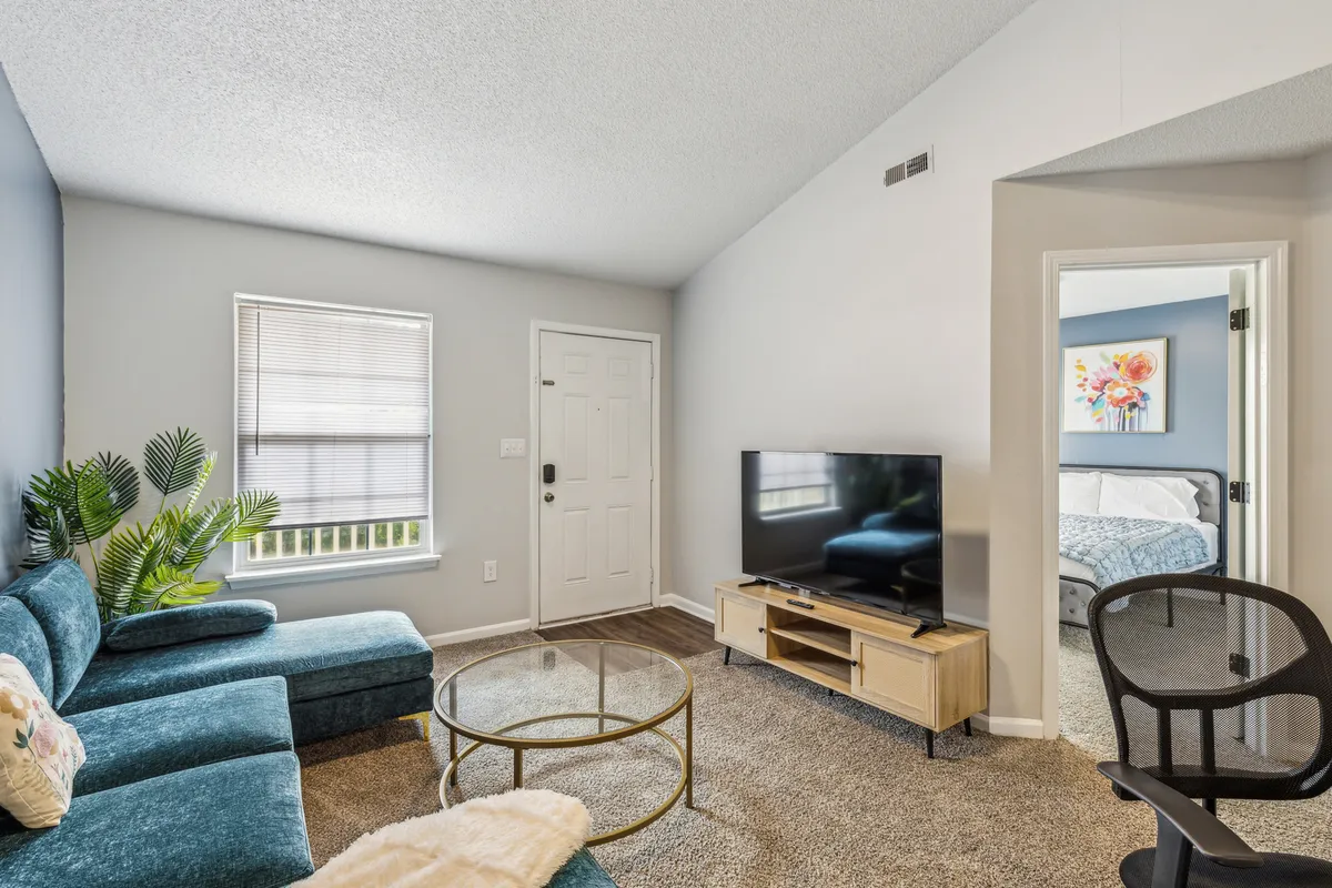 A cozy living room setup featuring a comfortable sofa and coffee table facing a television, with a doorway leading to adjacent spaces. The scene hints at evenings spent watching shows, hosting game nights, or simply relaxing after a busy day.