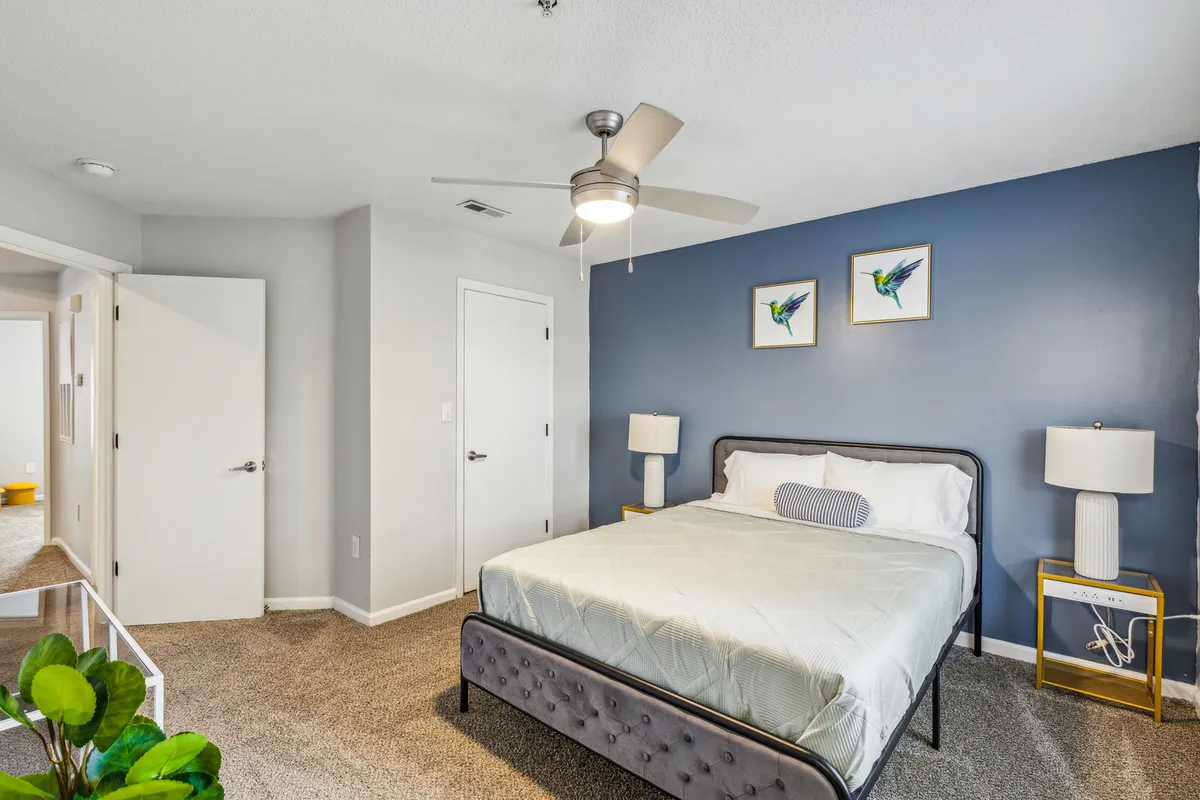 A modern bedroom with a plush bed, stylish blue accent wall, contemporary artwork, and inviting nightstands. The atmosphere is tranquil and conducive to a restful night's sleep or a peaceful morning routine.