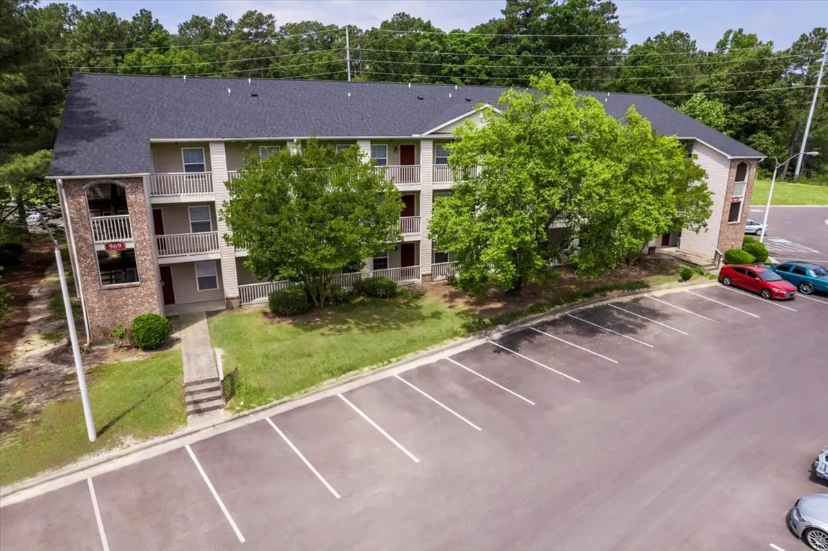This exterior shot highlights the building's welcoming facade, shaded by large trees, with open areas suitable for leisure walks, morning coffee, or afternoon picnics. The calm, homey atmosphere exudes a connection to nature right outside the door.