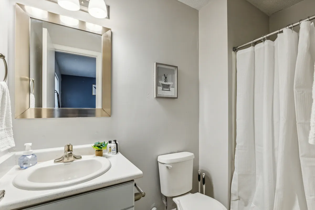 A modern bathroom featuring a large mirror over the sink, shower curtain, toilet, and calming wall art. The space feels clean, functional, and relaxing, ideal for both morning routines and evening unwinding.