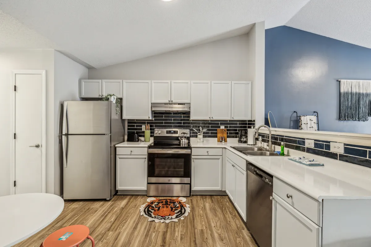 A cheerful, modern kitchen featuring stainless steel appliances, grey cabinetry, a playful tiger-themed rug, and a blue accent wall. The space is set up for both cooking and entertaining, with ample workspace and vibrant details that create a welcoming atmosphere for family gatherings.