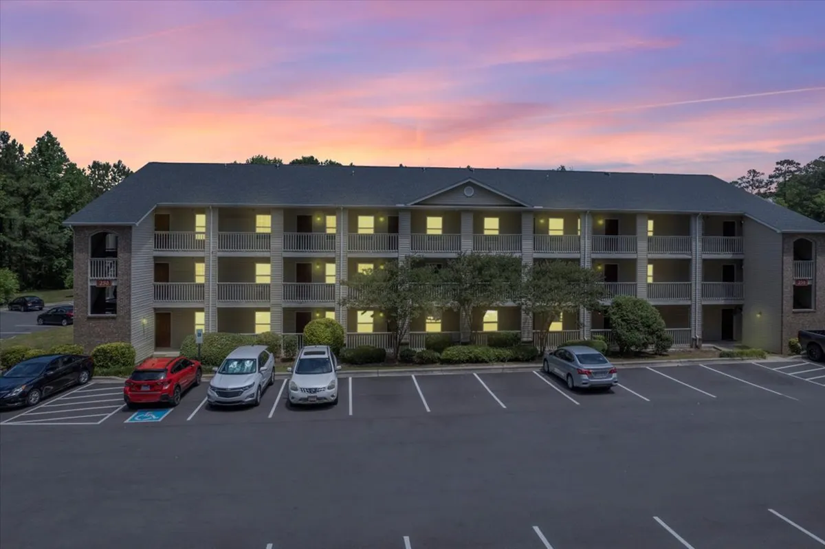 Captured at sunset, this exterior shot features the apartment building and parking lot, bathed in warm evening light. The sky’s colors and the spacious grounds evoke a sense of community life and evening relaxation after a day out in the city.